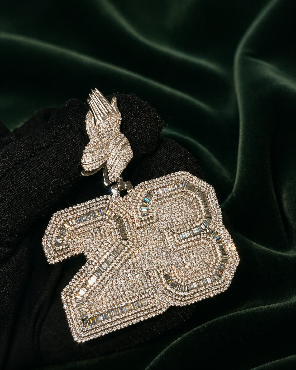 Custom 23 plate pendant with praying-hands cap, set in white gold and baguette diamonds, photographed on forest velvet.