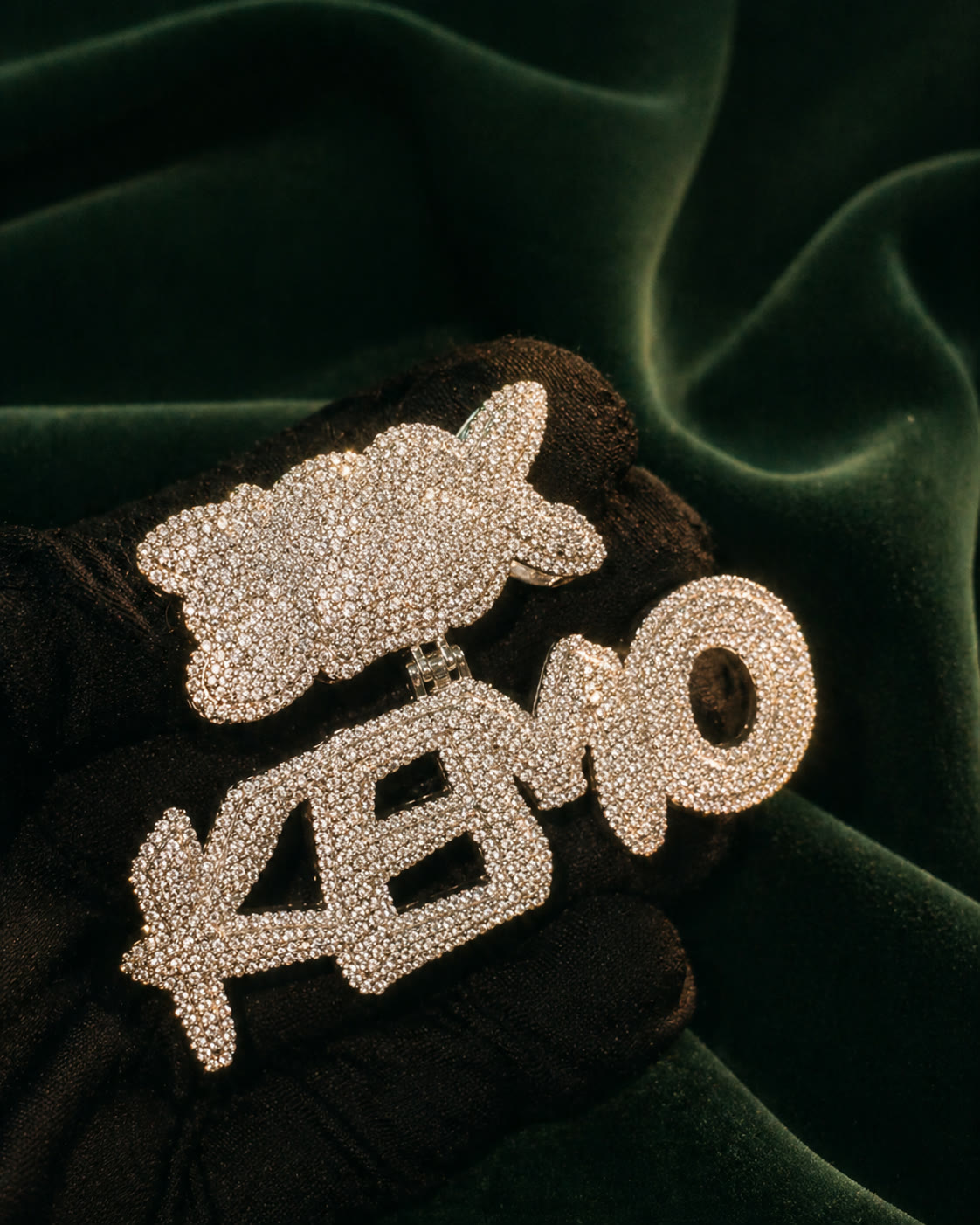 Custom KEMO monogram pendant in white gold, fully iced with round and baguette stones, on forest velvet.