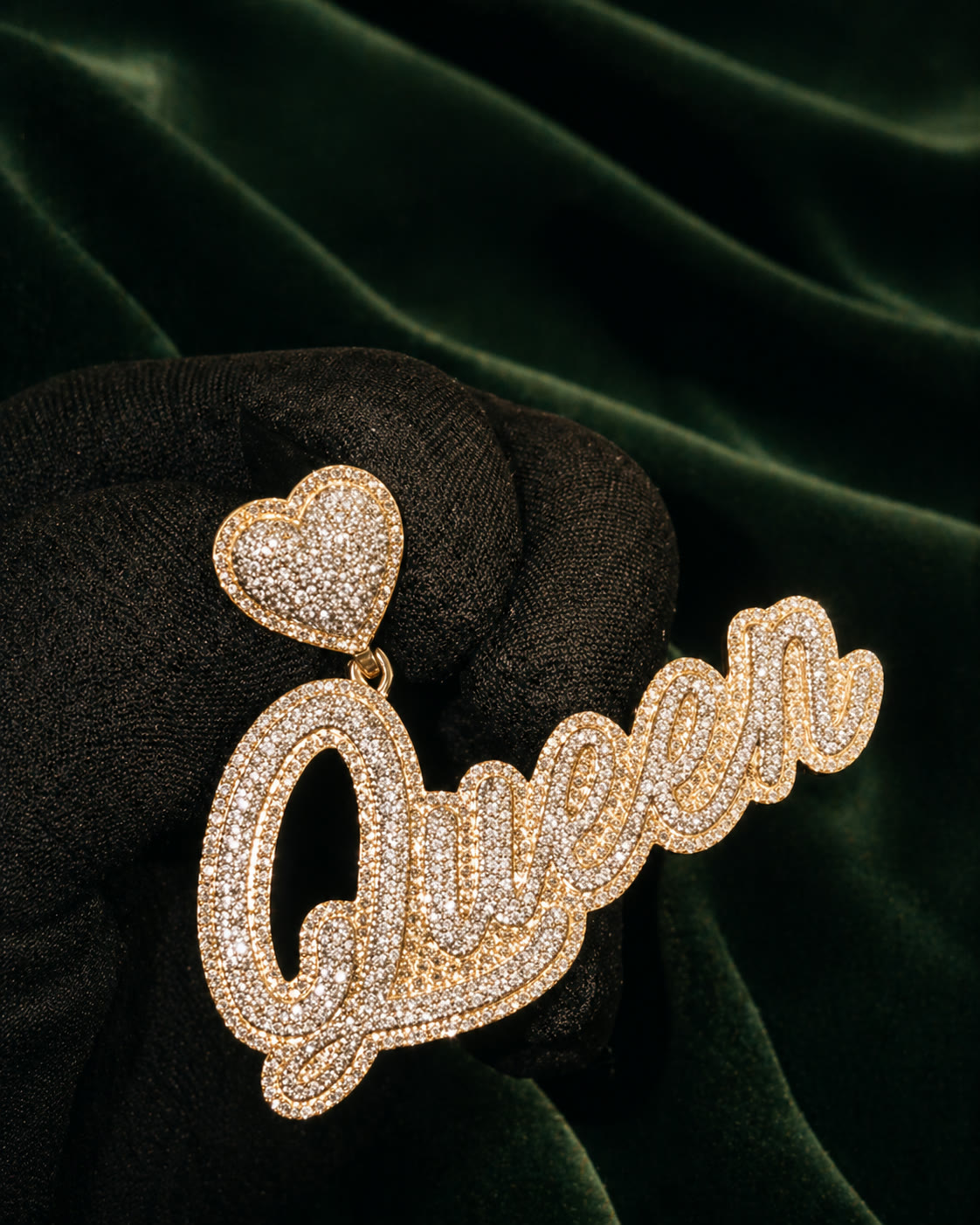 Custom Queen script pendant with heart drop, yellow gold and pavé diamonds, on forest velvet.