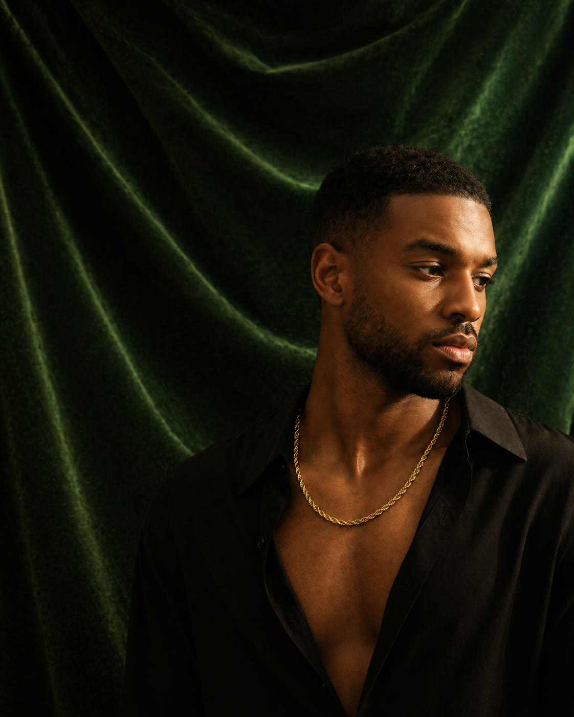 A man in a black open-collar shirt wearing a heavy gold rope chain, photographed against deep forest-green velvet — a frame from a Jewelry Aura custom commission.