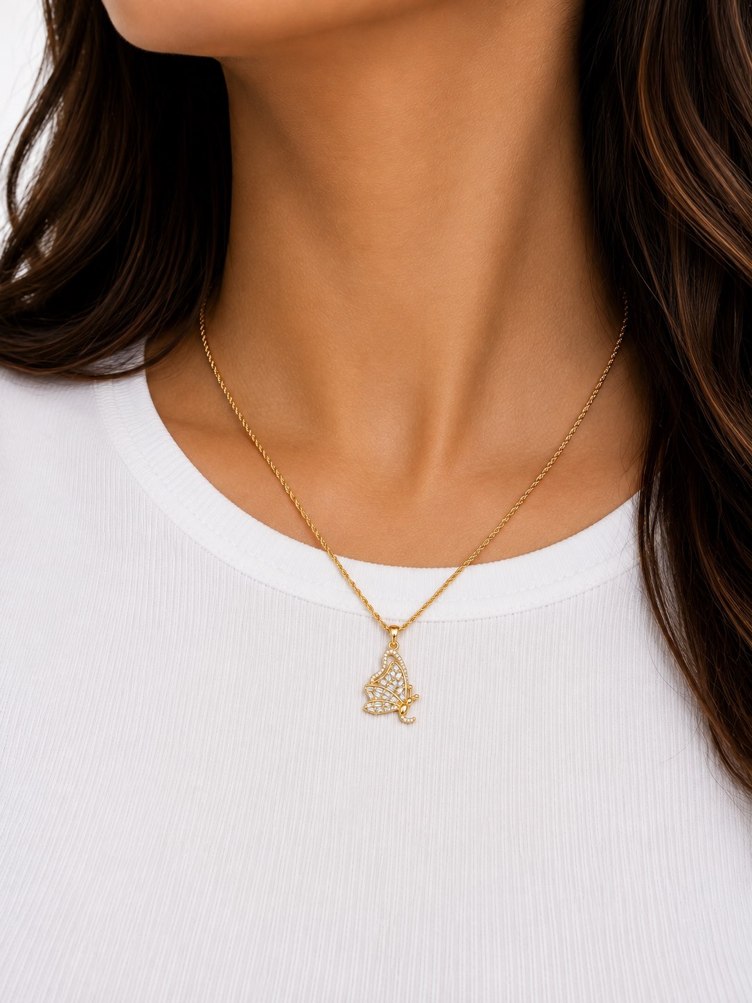 A gold rope chain and pavé butterfly pendant worn over a white tee.